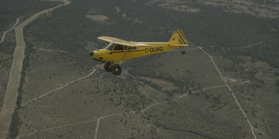 A small yellow single engine plane in flight