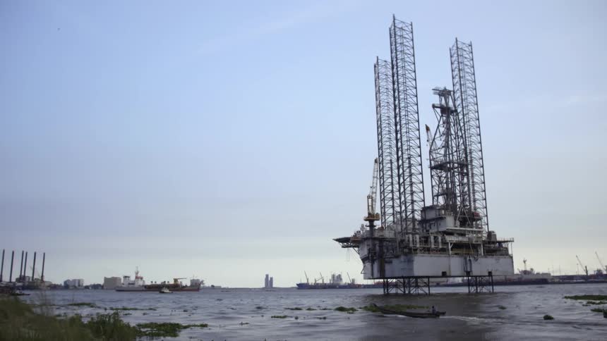 A small boat motors past rocks and a crane platform in a harbor