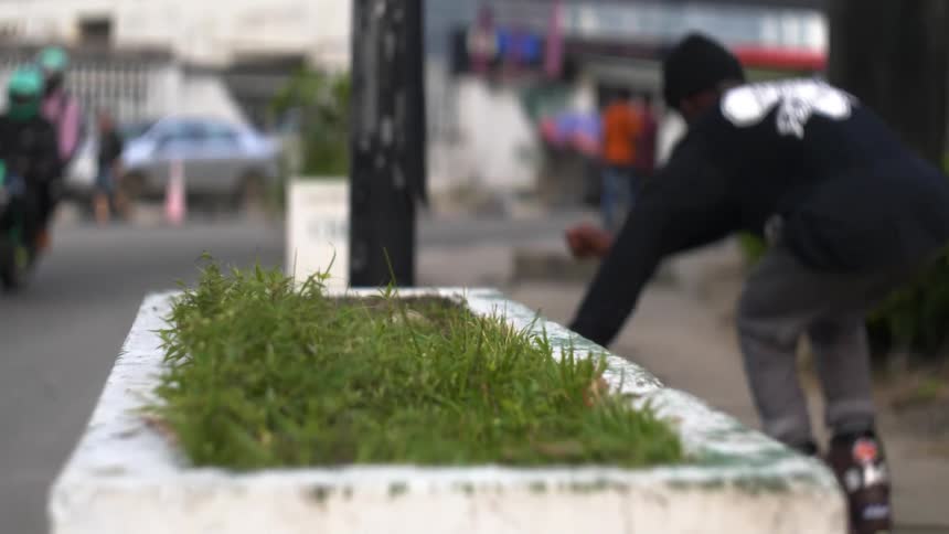 Inline skaters rides along edge of grass filled concrete potter near busy street