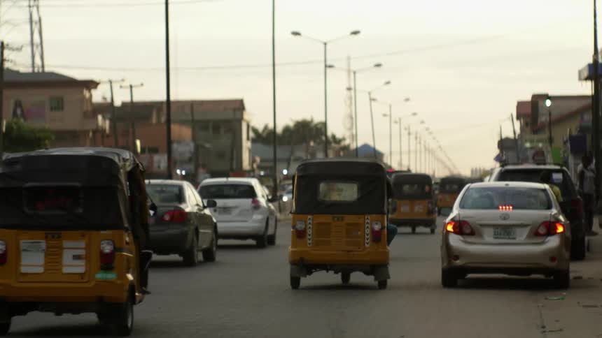 Cars and three wheeled taxis travel on a busy city street
