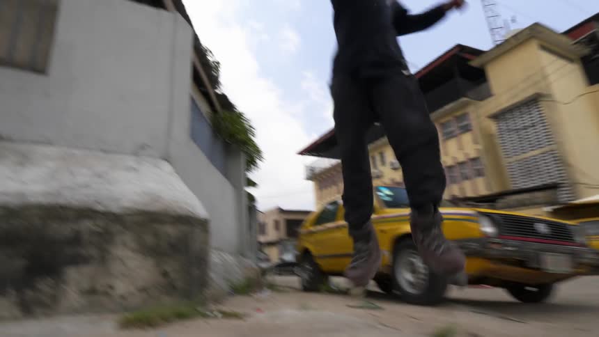 A young man roller skating in the middle of a road jumps up onto the side of a building slope and performs a twist stunt