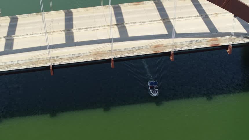 Boat driving under a bridge over the green waters of a river