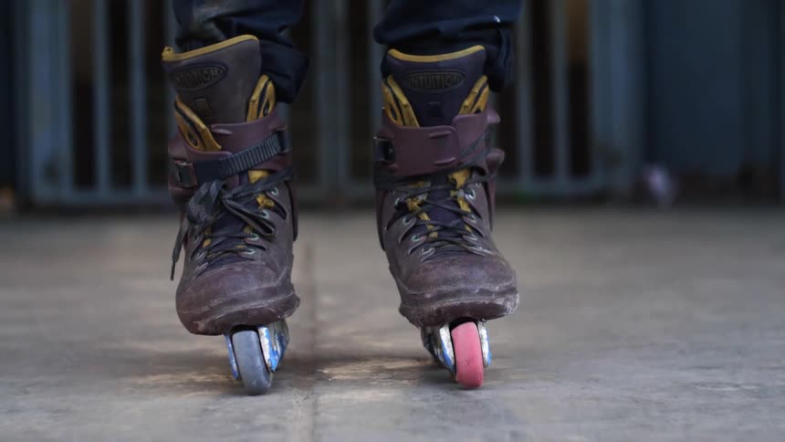 A person stands in place while wearing a pair of heavily used roller blades