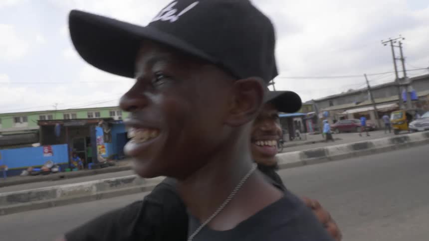 Two men with hats hugging and smiling with buildings the sky and clouds in the background
