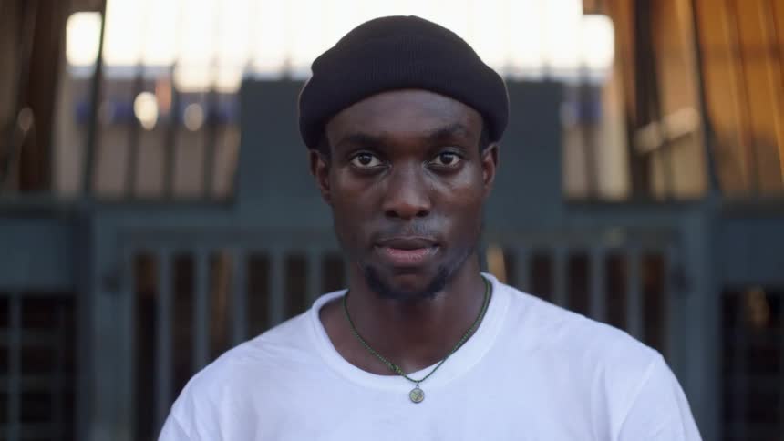 A man stands outdoors in front of a metal gate while looking directly at the camera