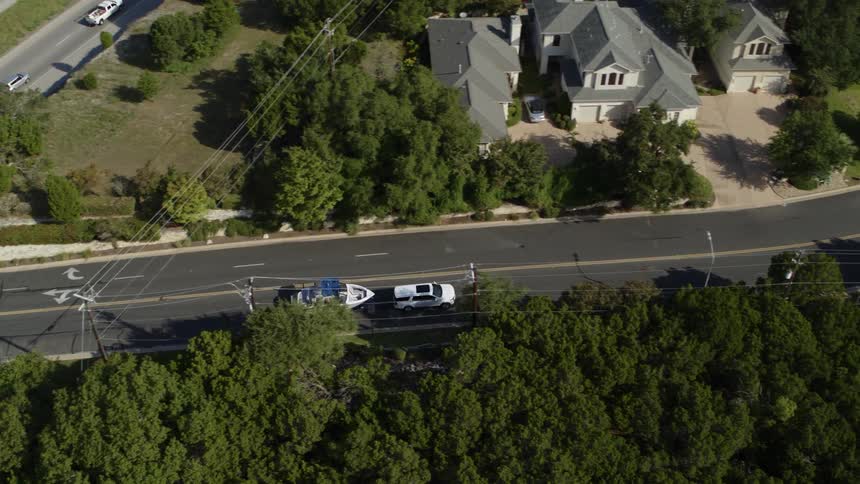 An suv pulls a boat behind it as it travels down a road during the day