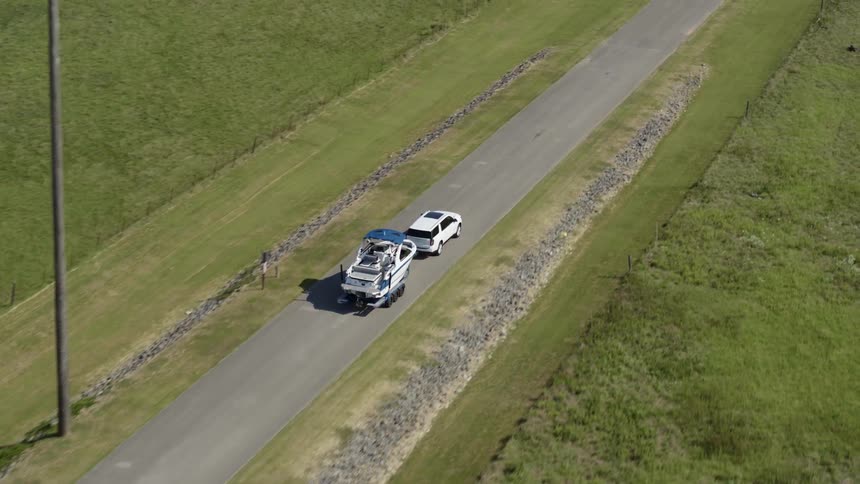 A white van travels down a road pulling a boat