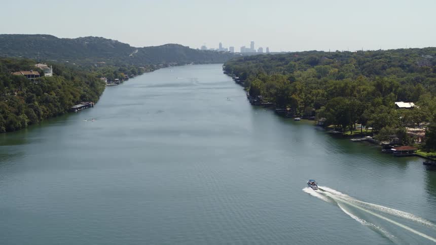 A boat travels down a river towards a distant metropolis during the day