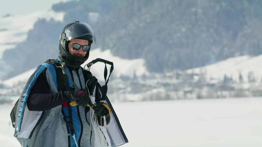 Parachutist threading parachute cords while standing in front of a mountain at winter