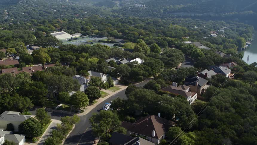 A car travels a road in a large neighborhood of homes and trees