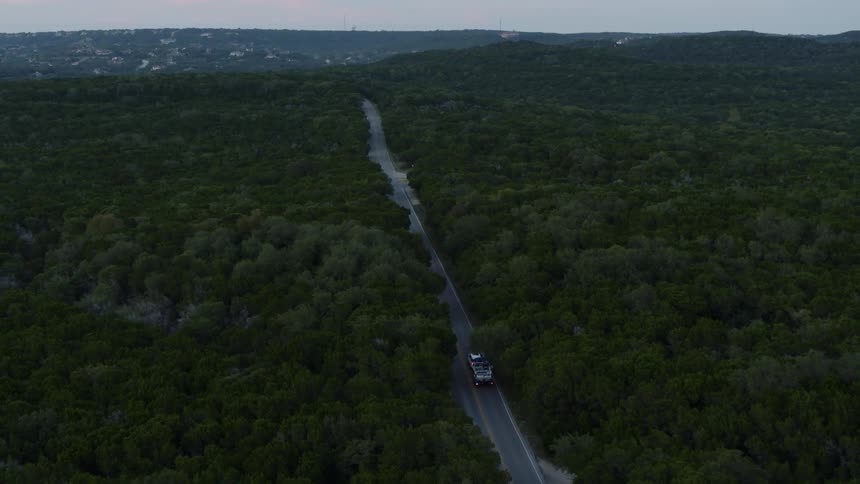 A vehicle driving on a road surrounded by trees with the sky and clouds in the background