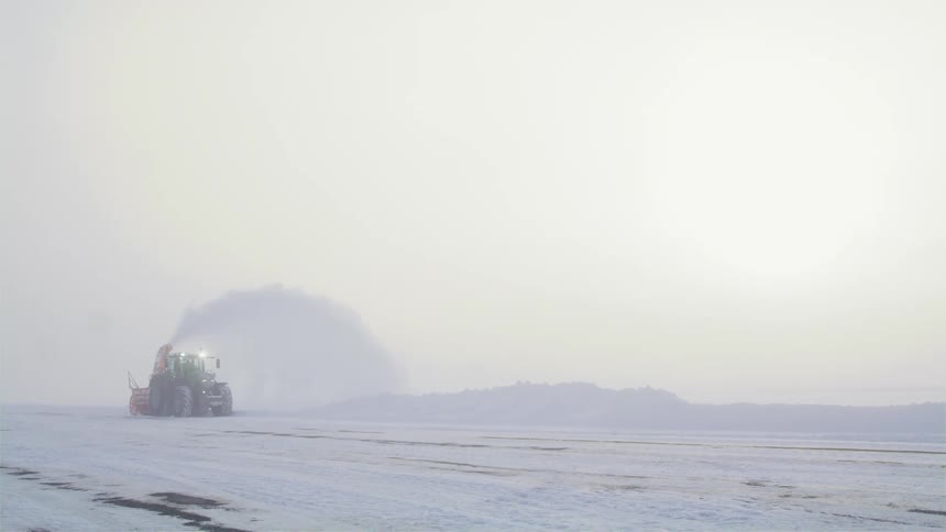 A snow plow moves across a snowy road next to a field