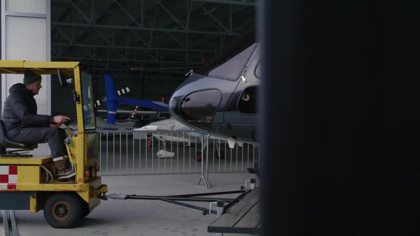 A man slowly tows a helicopter out of a hangar