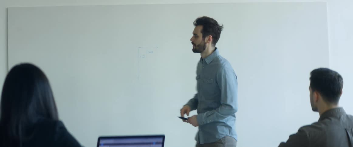 A professor writes on a white board as he talks to students