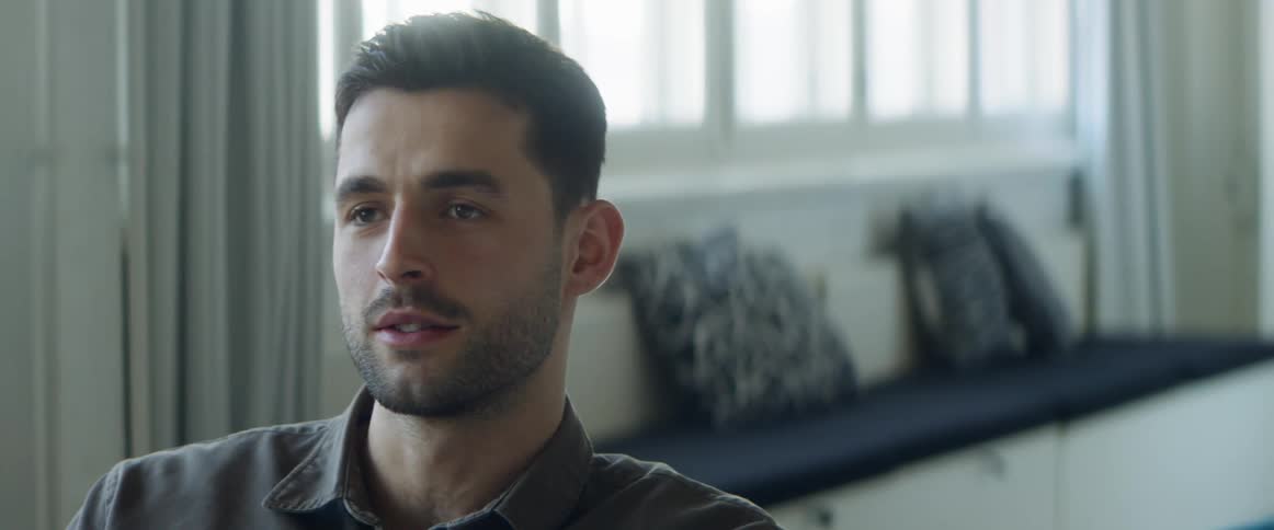 A man with a shirt in a room with a wall and window in the background