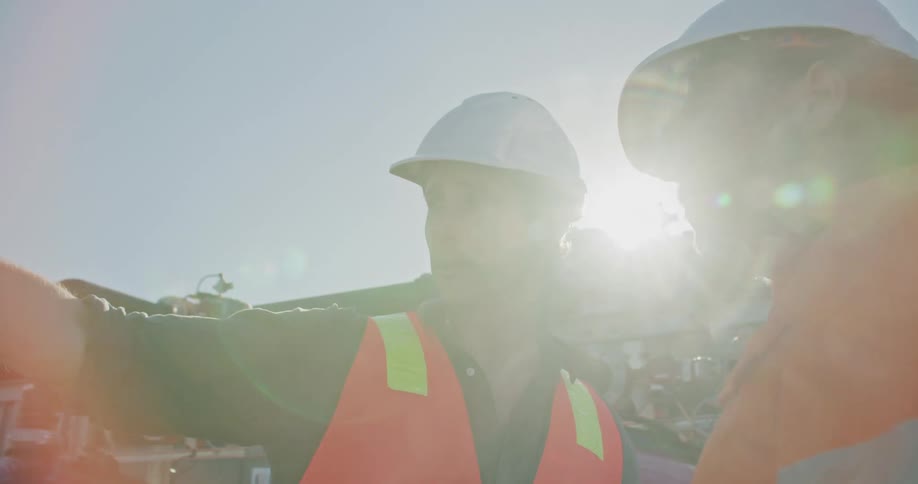 Two men with hardhats standing with pipes the sky and clouds in the background
