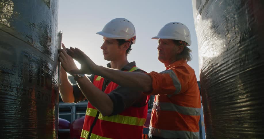 Two workers looking at pipes outdoors