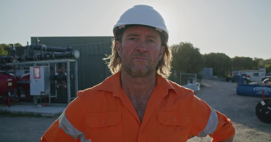 A man with a hardhat with pipes trees the sky and clouds in the background