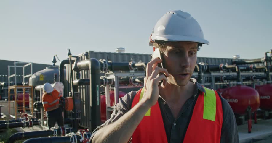 A man stands in front of machinery and talks on a cell phone as another man inspects the machines