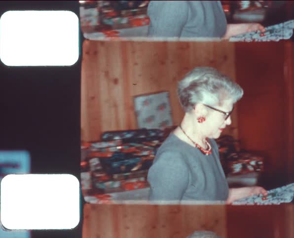A woman with glasses in a room holding a present with a wall and stairway in the background