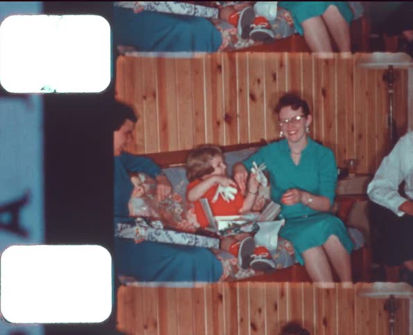 A child opening presents on a couch surrounded by family