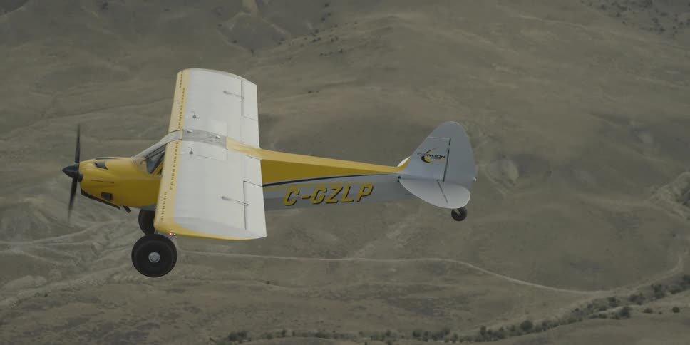 A yellow plane flies over a desert