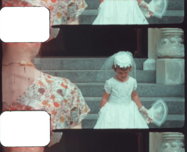 A little girl holding a bouquet of flowers standing on a staircase outdoors while a man and a woman watch