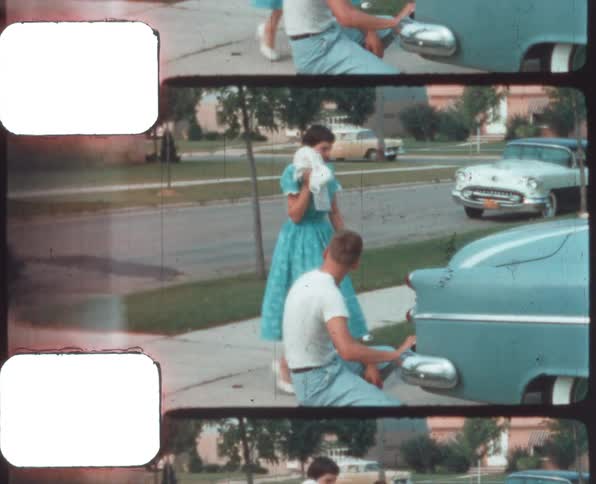 Woman walks to a man crouching near a parked car caught on vintage film