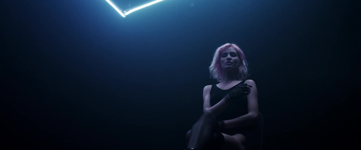 Young woman with pink hair looking at the camera on a dark room under blue neon lights