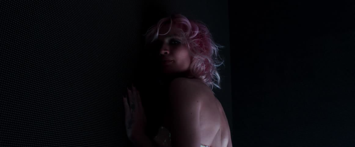 A woman with short blond hair stands in a darkened room while posing for the camera