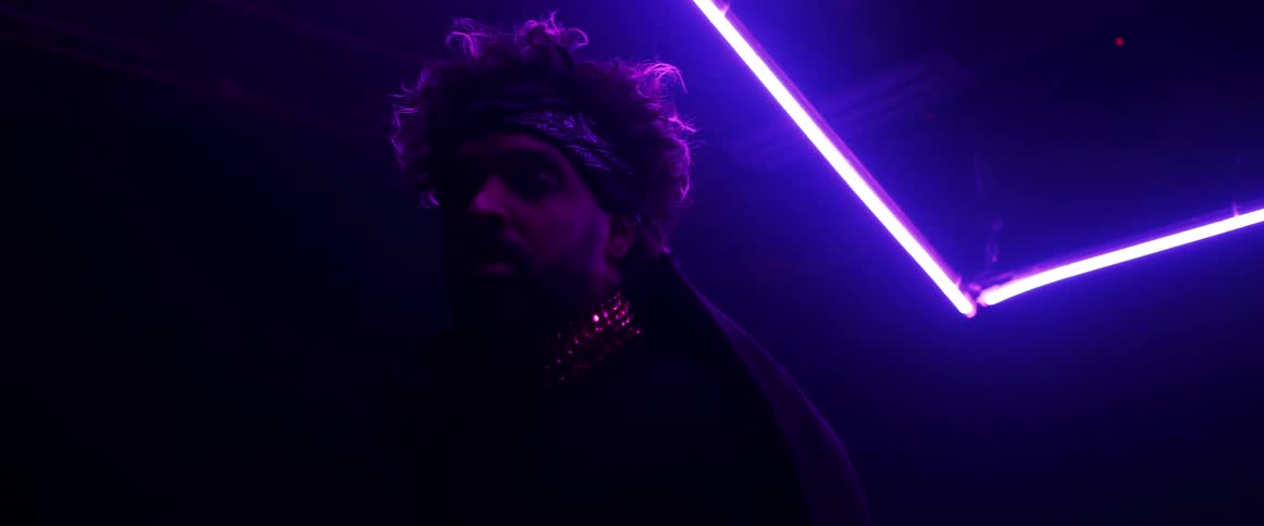 Man wearing a head band dancing on a dark room under magenta neon lights