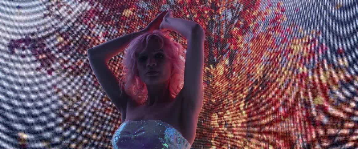 A woman with blonde hair poses in front of a large screen displaying images of trees