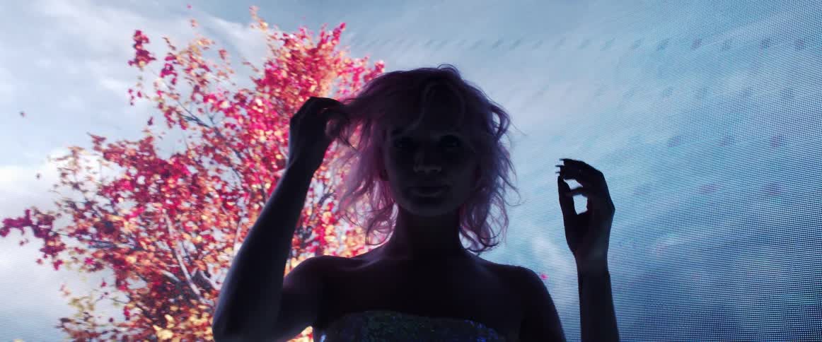 Young woman with pink hair looking at the camera on a dark room in front of a digital display