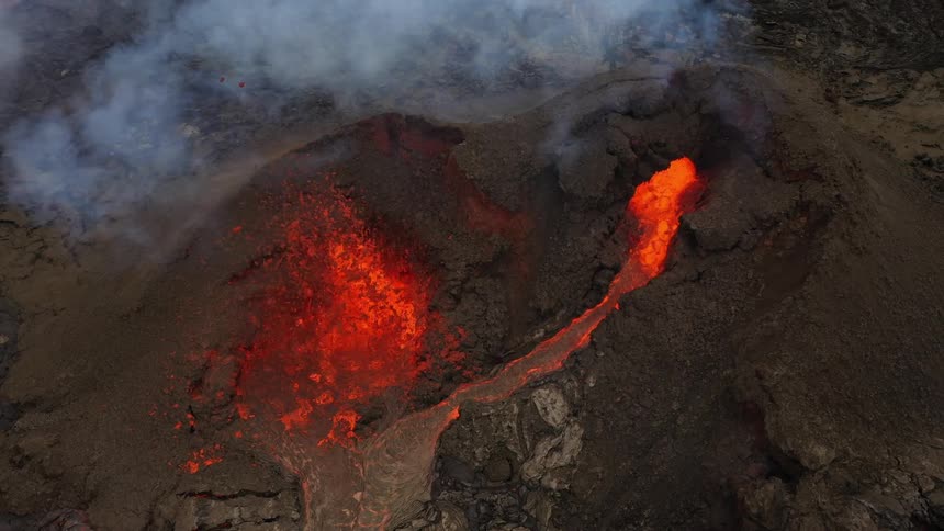 Erupting volcano spews molten hot lava into the air and oozes a river of hot lava