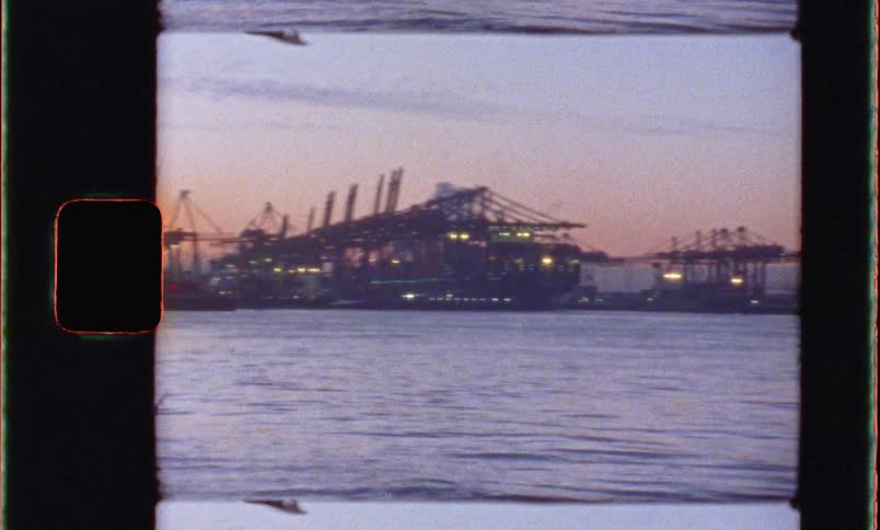 A shipyard lined with container cranes at sunset