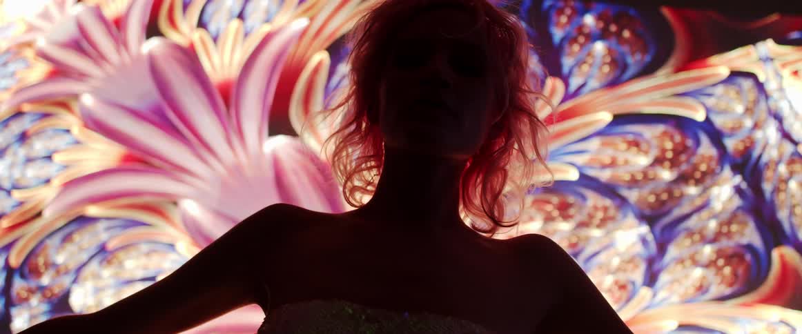A model poses in front of a digital screen with a colorful psychedelic pattern