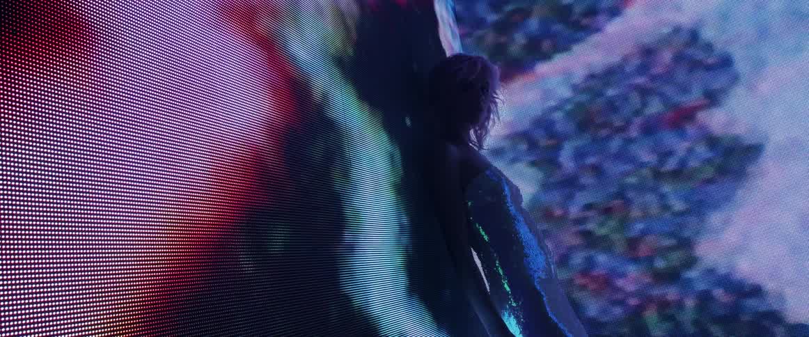 A model in a sequin dress poses in front of a large screen showing digital graphics