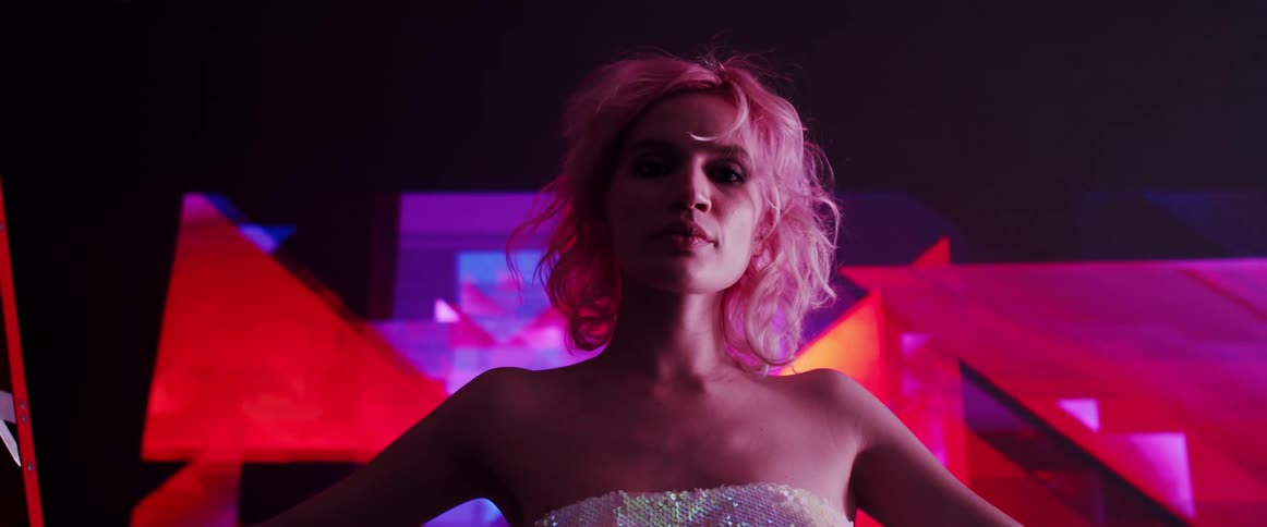 A woman stands indoors in front of a large screen displaying colorful abstract graphics