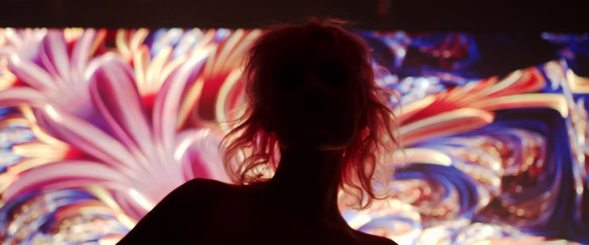 Young woman with pink hair looking at the camera on a dark room in front of a digital display