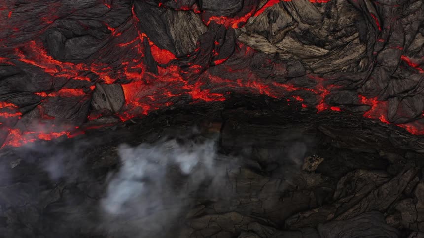 As a volcano erupts there is a large amount of glowing molten lava flowing out of it