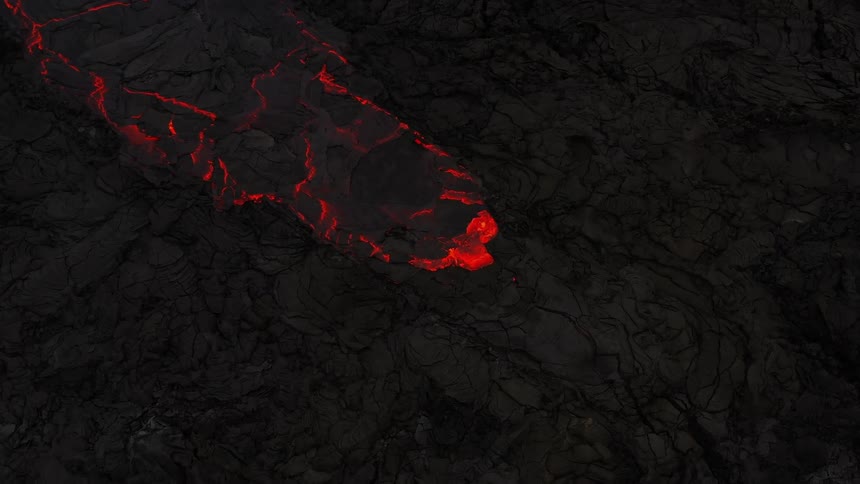 As a volcano erupts there is glowing hot lava slowing flowing down it