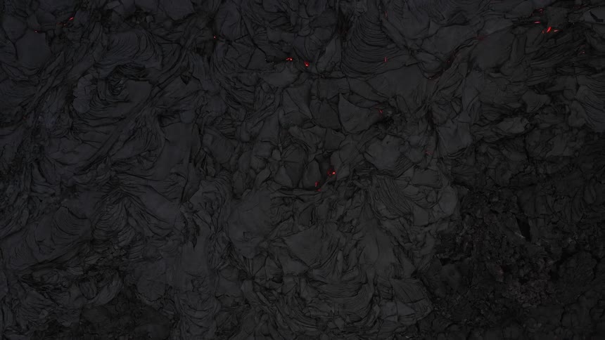 Aerial view of hardened lava near an erupting volcano