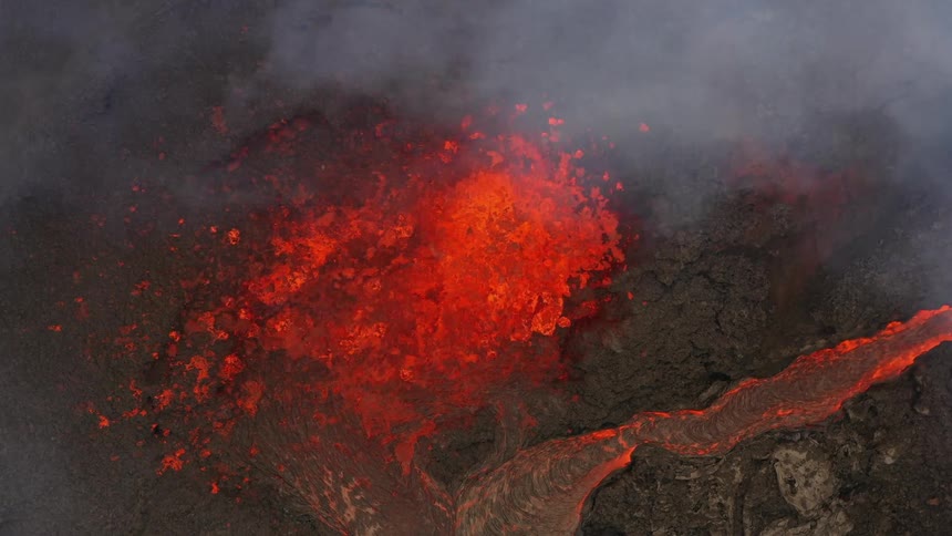 Erupting volcano spews molten hot lava into the air and oozes a river of hot lava