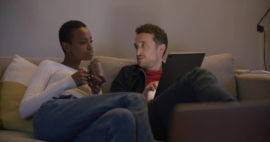 A man and a woman in a room sitting on a couch and looking at a tablet