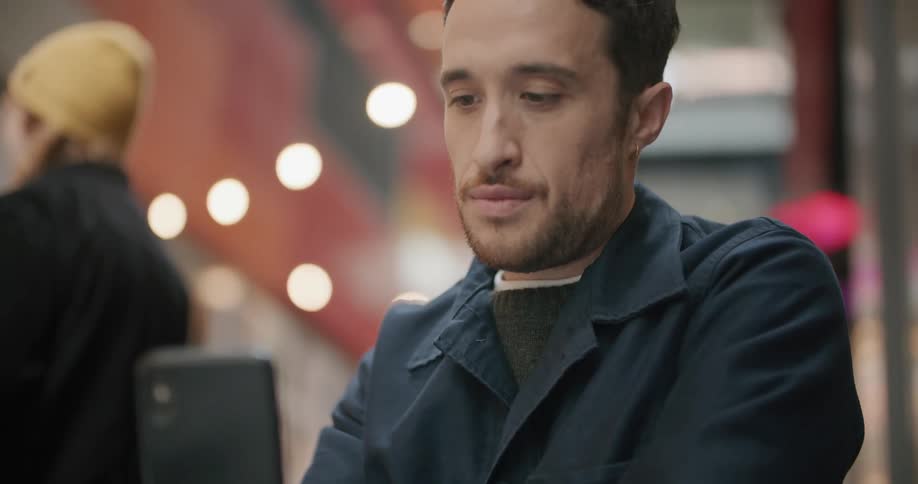 A man sits at a table outside a restaurant and uses his cell phone