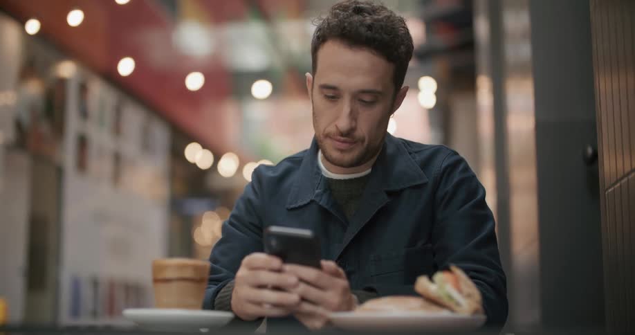 A man sits at a table at a restaurant and looks at his cell phone