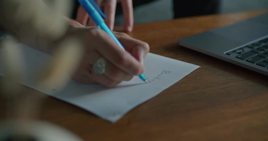 Woman with a ring writes in a paper and uses a grey laptop