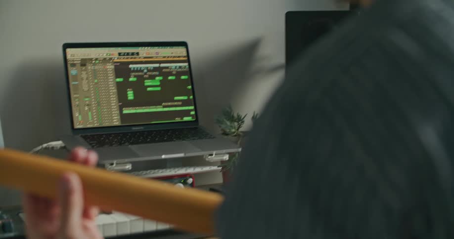 A man uses a laptop to record as he plays an electric guitar while sitting indoors during the day