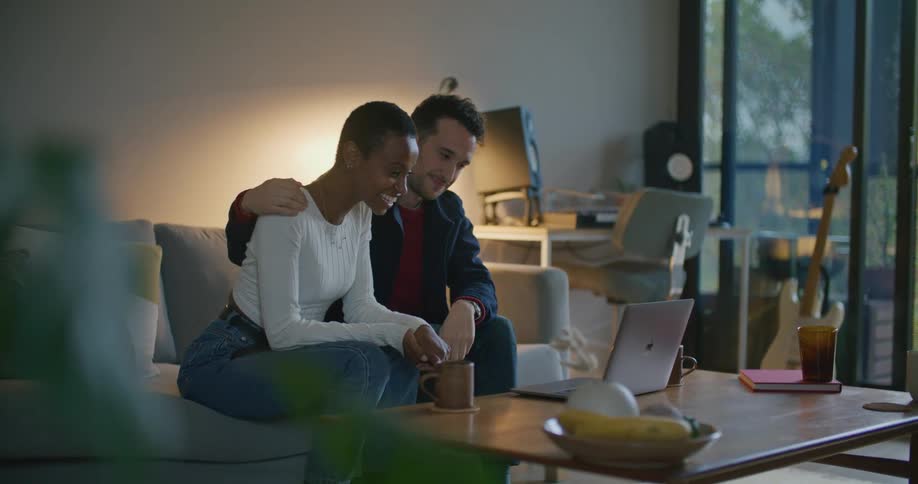Young couple sitting on the living room talking on a video conference in front of a laptop over the coffee table