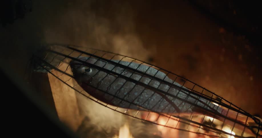 A fish cooking over open flames outside